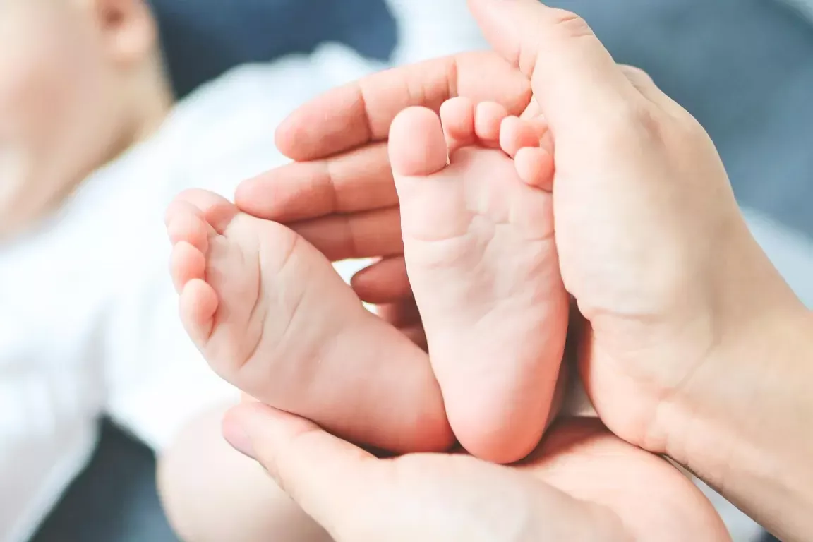 Zwei Frauenhände die die Füße eines Säuglings halten